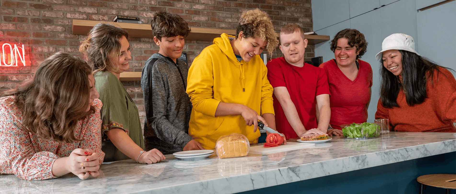 Four Best Buddies participants are gathered around a kitchen island. One of them is slicing a tomato.